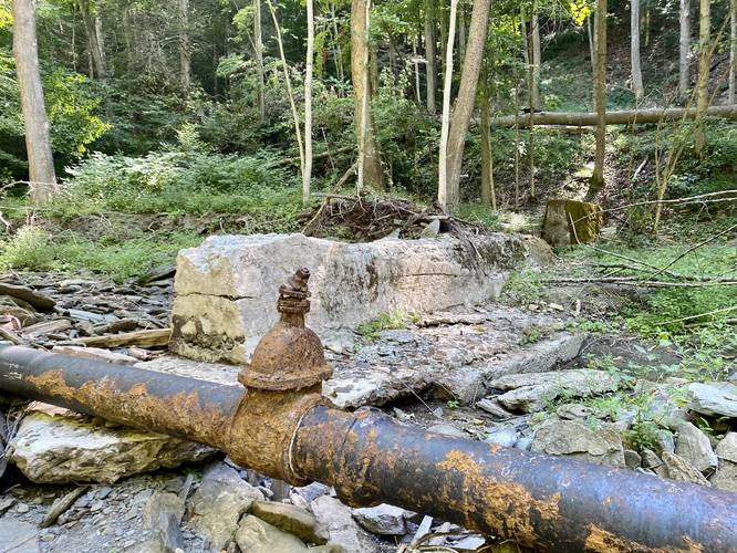 Old splash dam from logging era with large metal piping, likely to fill water tanks for trian cars